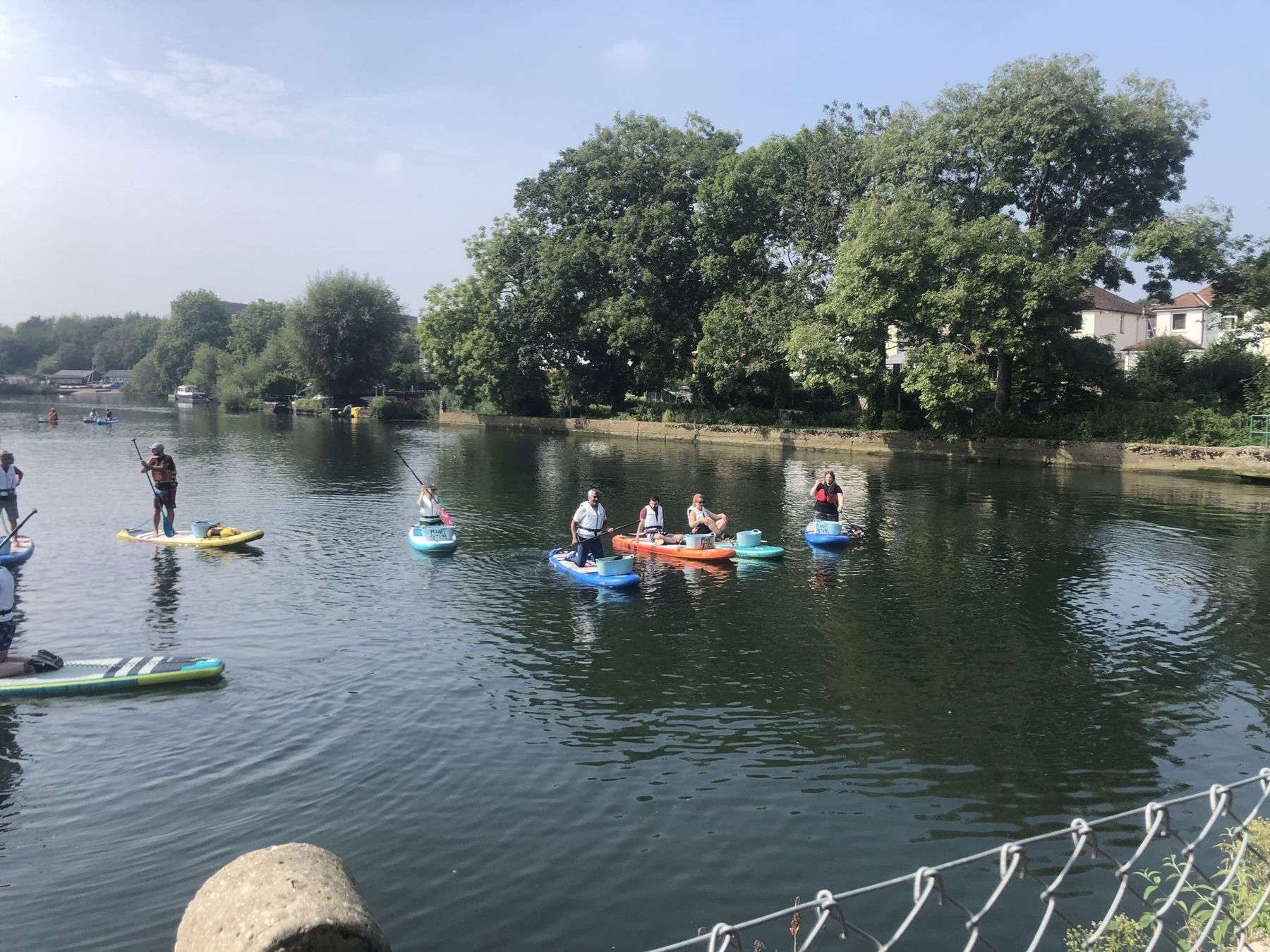 Paddleboarders spread across the river, each with a bucket, collecting litter