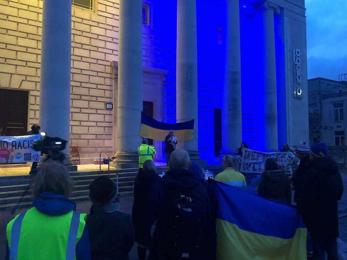Crowds with Ukrainian flags gathered at dusk outside Southampton Guildhall, lit blue and yellow, for the Peace Vigil for Ukraine